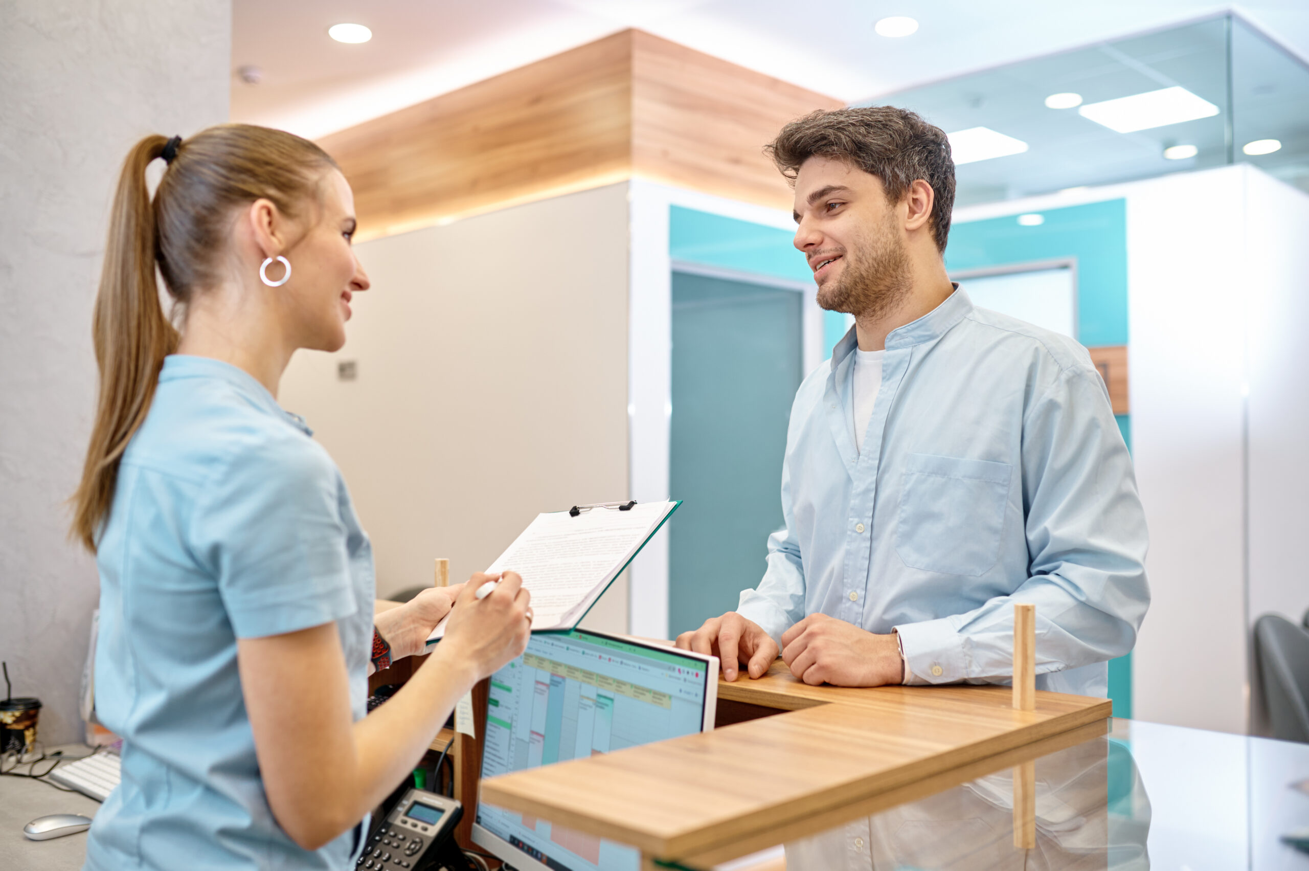 Man visitor talking to professional female receptionist at counter desk in modern clinic